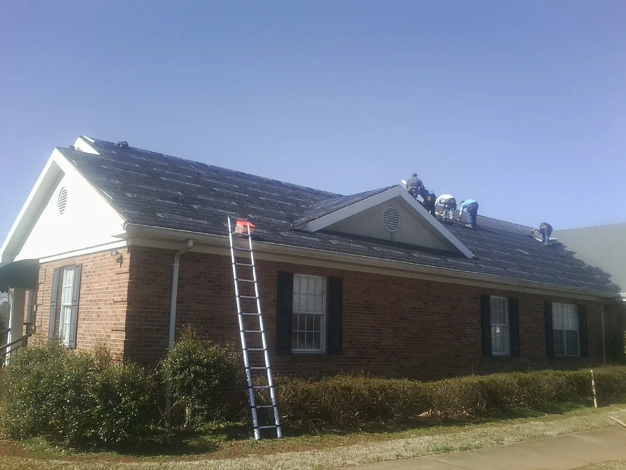 Crew tearing shingles off a brick ranch roof with a ladder set — Emergency Roof Repair work by our crew in East Pittsburgh