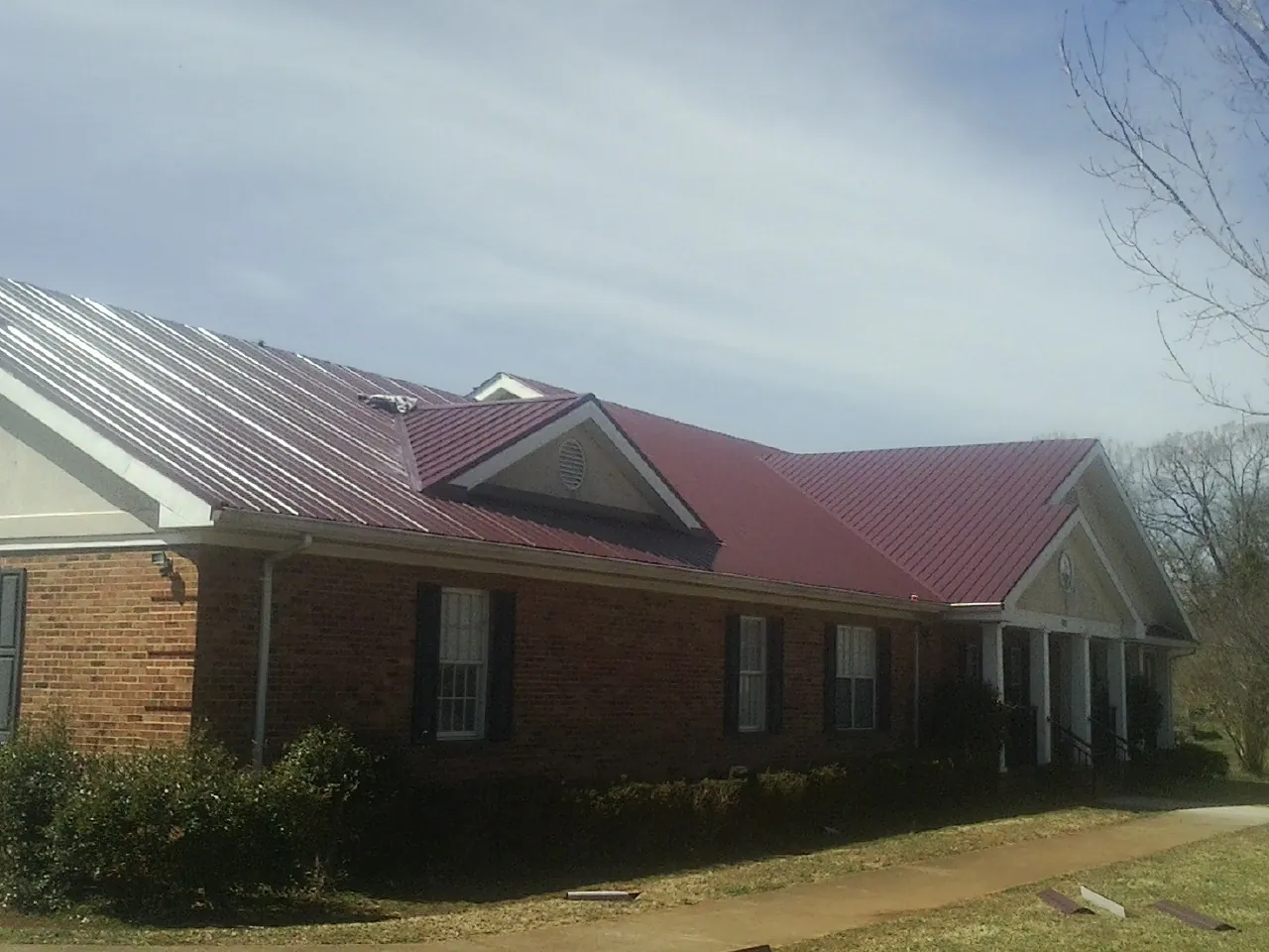 Red metal roof with gabled entries on a long brick building, from a Hail Damage Roof Repair job in East Pittsburgh