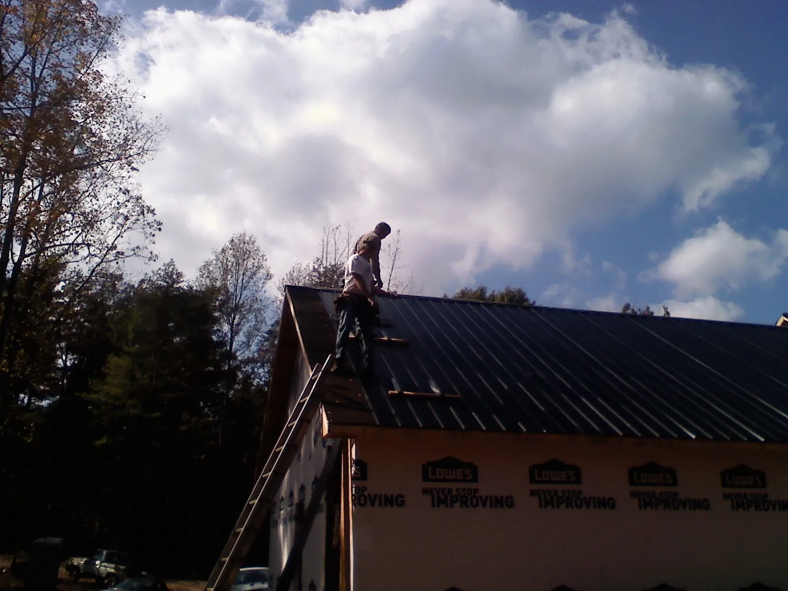 Roofer fastening dark metal panels high against a cloudy sky, from a Roof Inspection job in East Pittsburgh