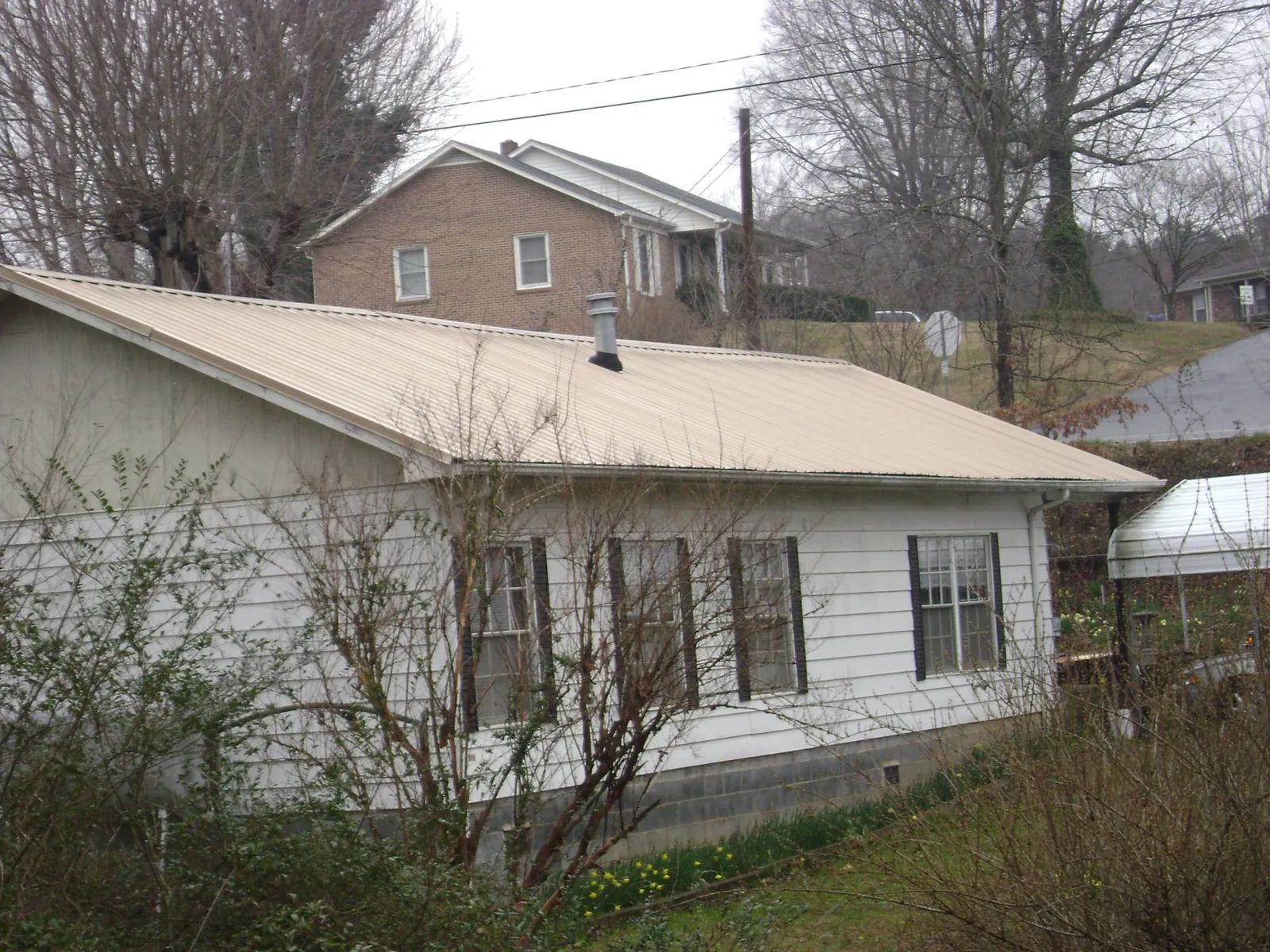 Tan metal roof on a white sided house set into a hillside — Commercial Roofing by Roofing Brothers in East Pittsburgh